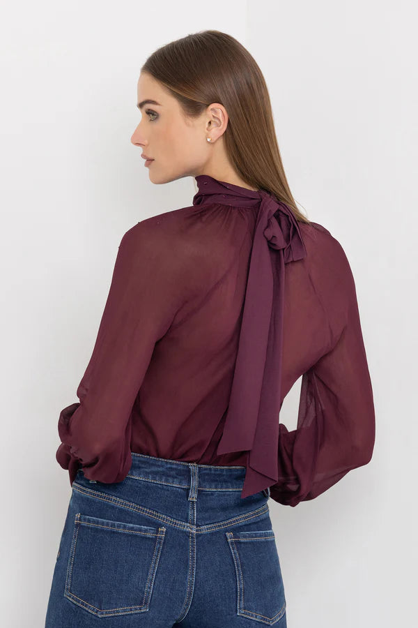 Woman wearing a burgundy blouse with tied neck and crystal embellishments against a white background