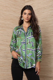 A woman modeling a green silk button-up shirt with an abstract blue, white, and gold chain pattern.