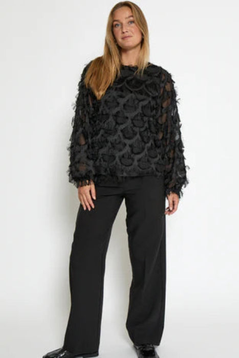 Woman wearing a black patterned top and black pants on a white background