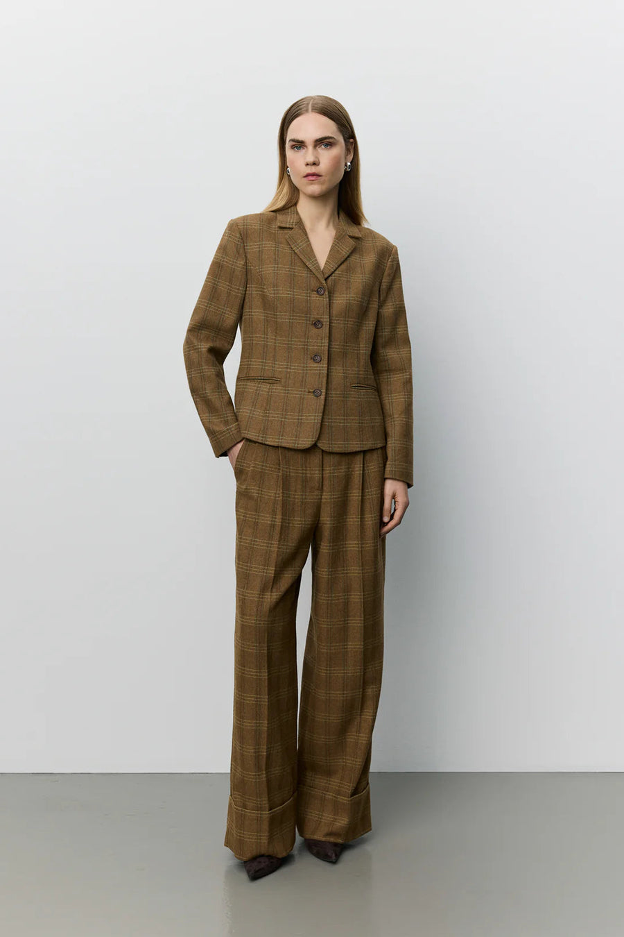 A woman modeling a brown plaid blazer with a double-breasted button closure and notch lapels. 