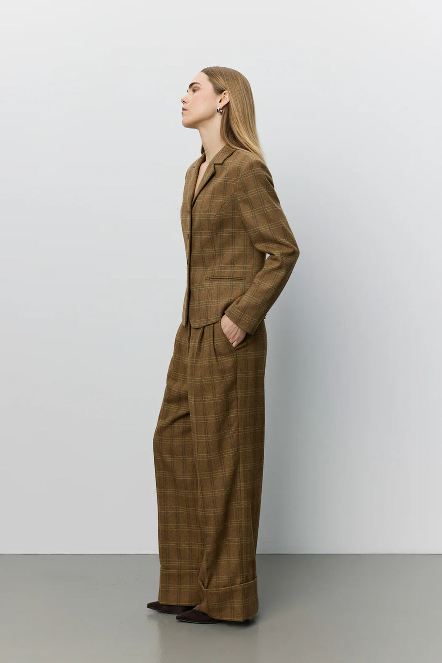 A woman modeling a brown plaid blazer with a double-breasted button closure and notch lapels. 