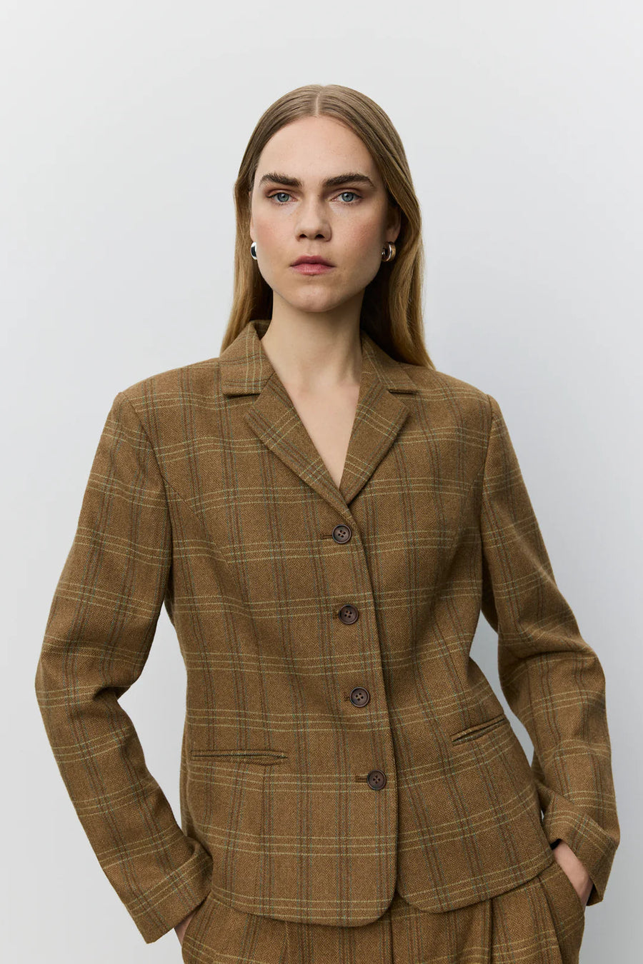 A woman modeling a brown plaid blazer with a double-breasted button closure and notch lapels. 