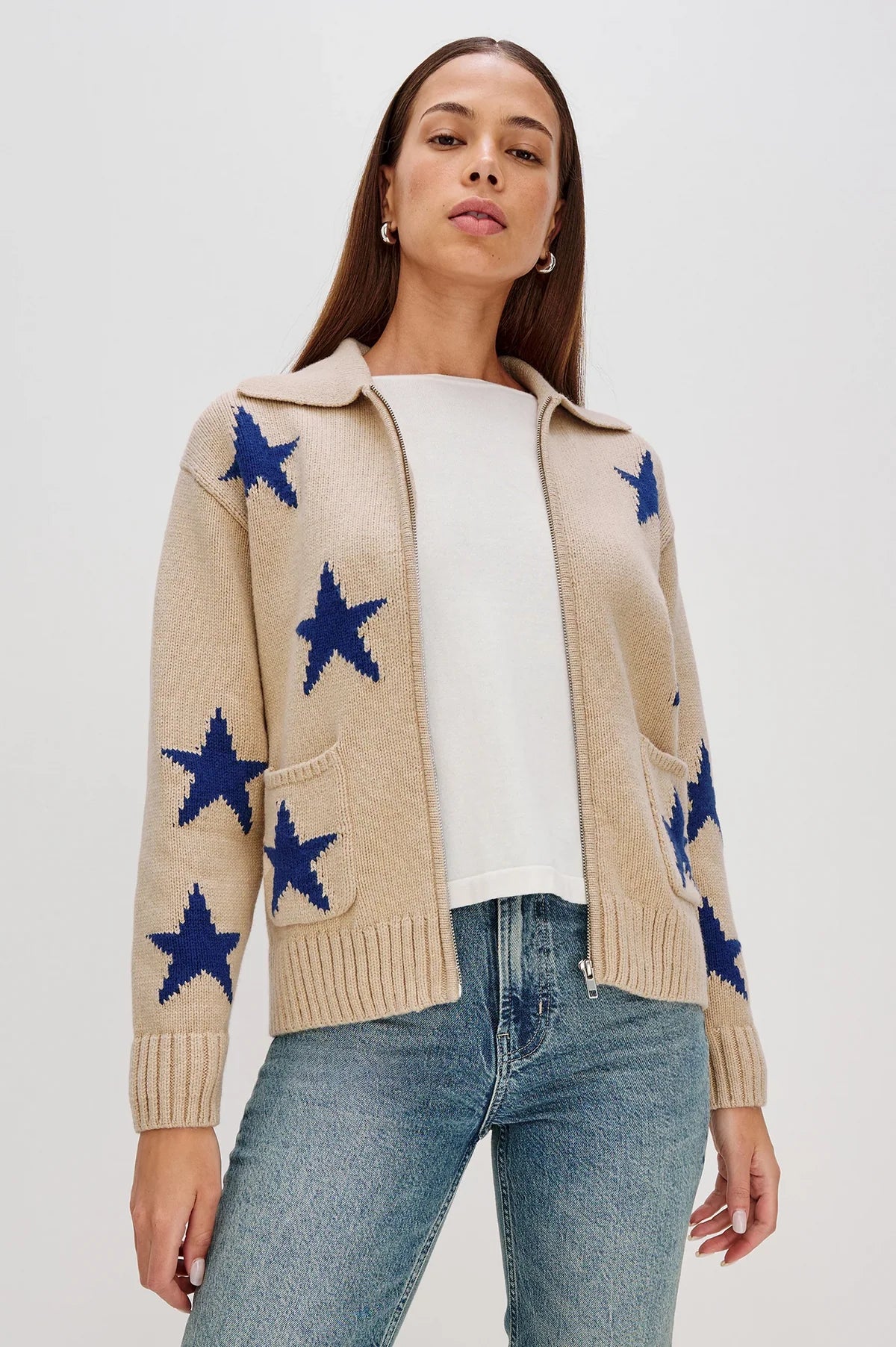 Woman wearing a beige zip-up sweater with blue star patterns and front pockets unzipped