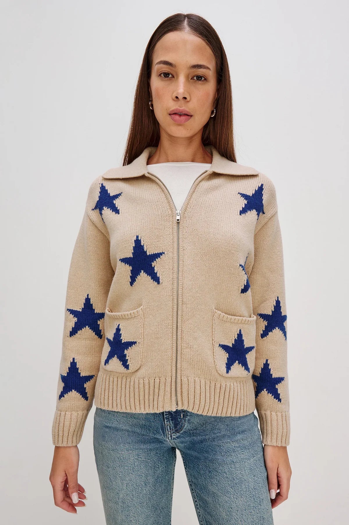  Woman wearing a beige zip-up sweater with blue star patterns and front pockets zipped up