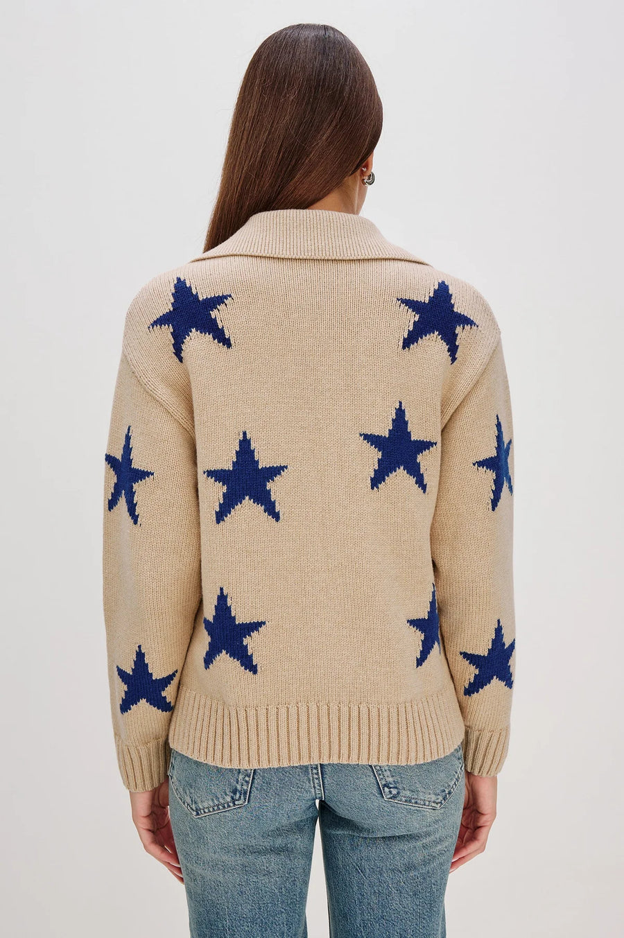 Back view of a woman wearing a beige zip-up sweater with blue star patterns and front pockets