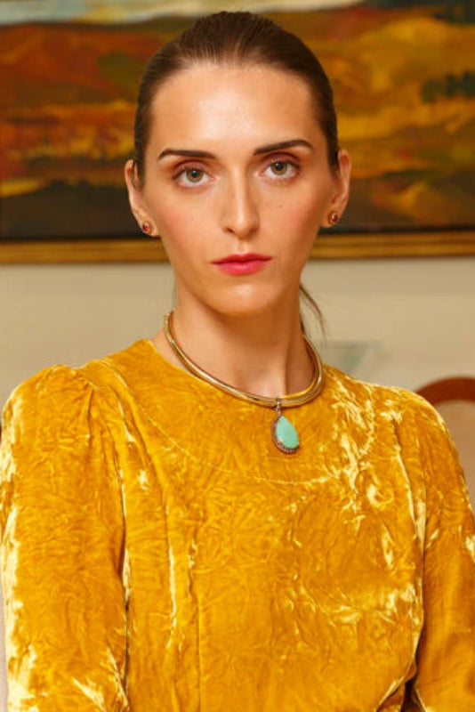 Woman wearing a yellow textured dress with a necklace in an indoor setting.