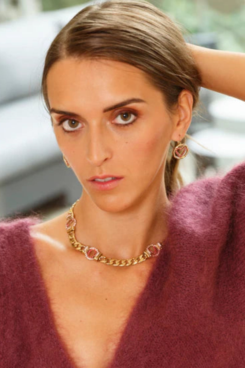 Woman wearing a gold necklace and earrings with a blurred background