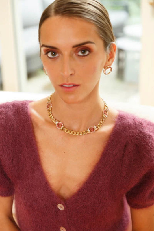 Woman wearing a purple cardigan and gold necklace indoors