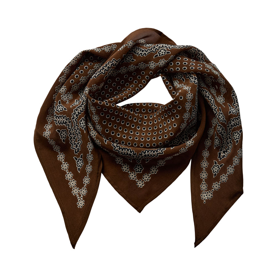 A brown square scarf with a white and gray paisley bandana pattern, styled in a loose knot on a solid white background.