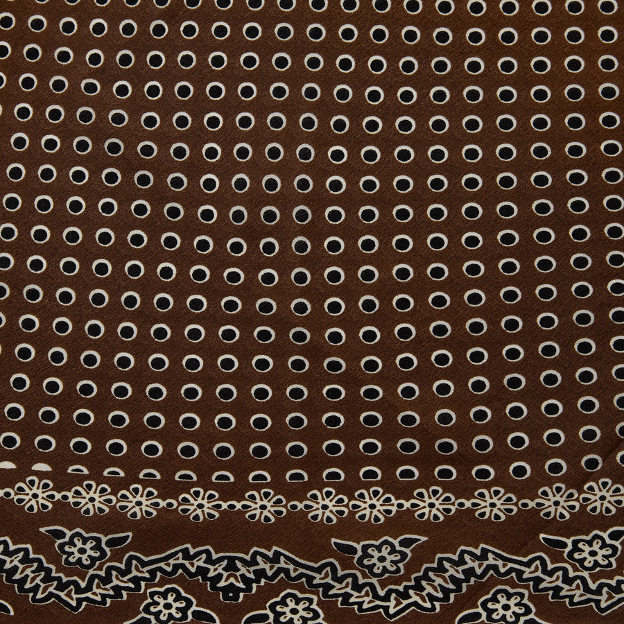 A brown square scarf with a white and gray paisley bandana pattern, styled in a loose knot on a solid white background.