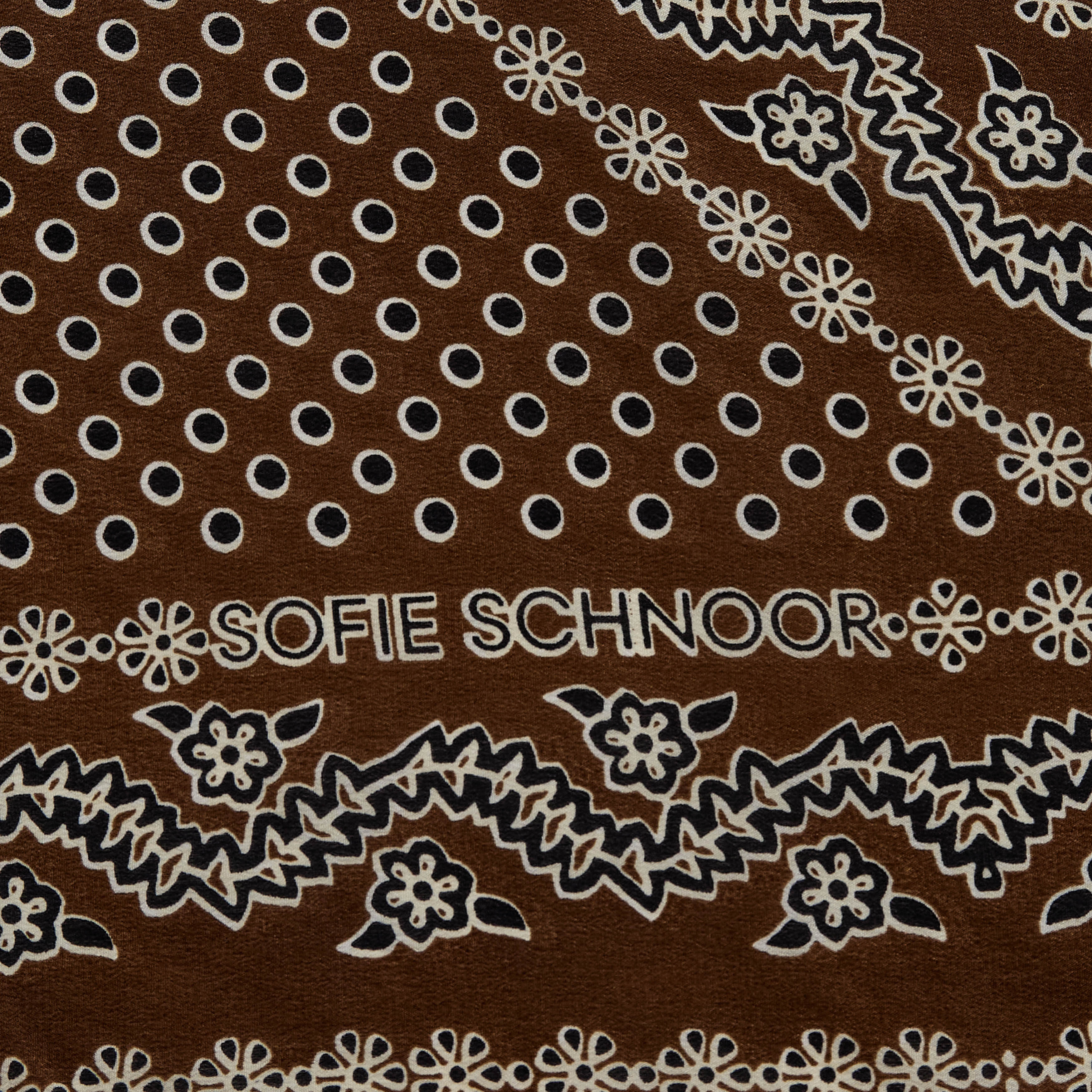 A brown square scarf with a white and gray paisley bandana pattern, styled in a loose knot on a solid white background.