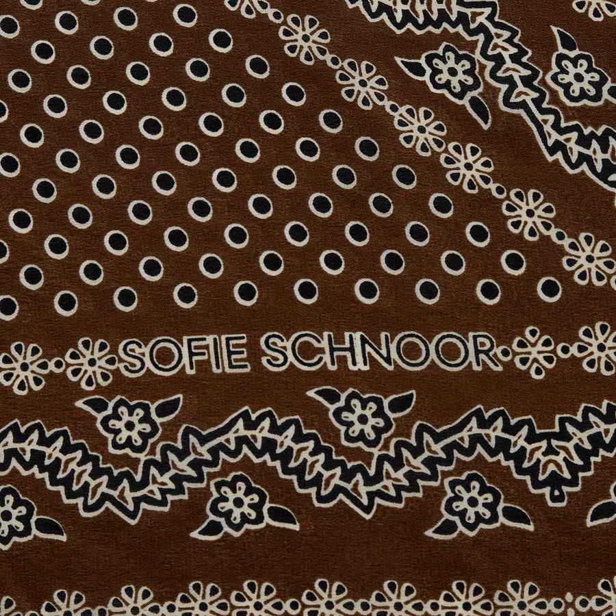 A brown square scarf with a white and gray paisley bandana pattern, styled in a loose knot on a solid white background.