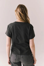 Back view of a woman wearing a black t-shirt with pink graphic design on a plain background