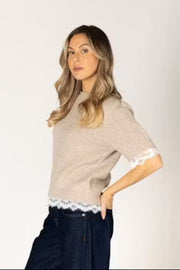 Woman wearing a beige sweater with lace trim. 