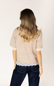 Woman wearing a beige sweater with lace trim. 
