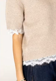 Woman wearing a beige sweater with lace trim. 