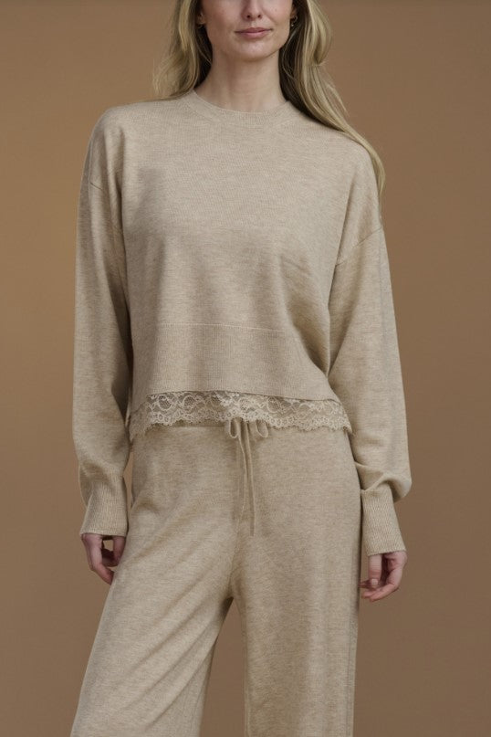 Woman wearing a beige sweater with lace trim. 