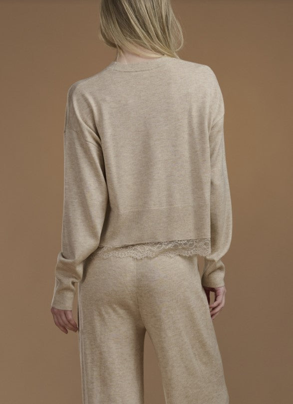 Woman wearing a beige sweater with lace trim. 