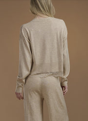Woman wearing a beige sweater with lace trim. 