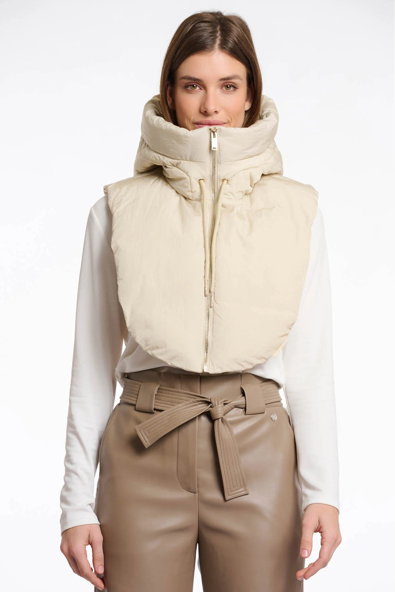 Woman wearing a beige puffer hood collar over a white shirt and brown pants on a white background
