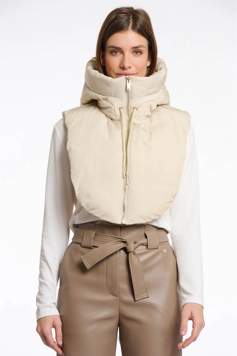 Woman wearing a beige puffer hood collar over a white shirt and brown pants on a white background