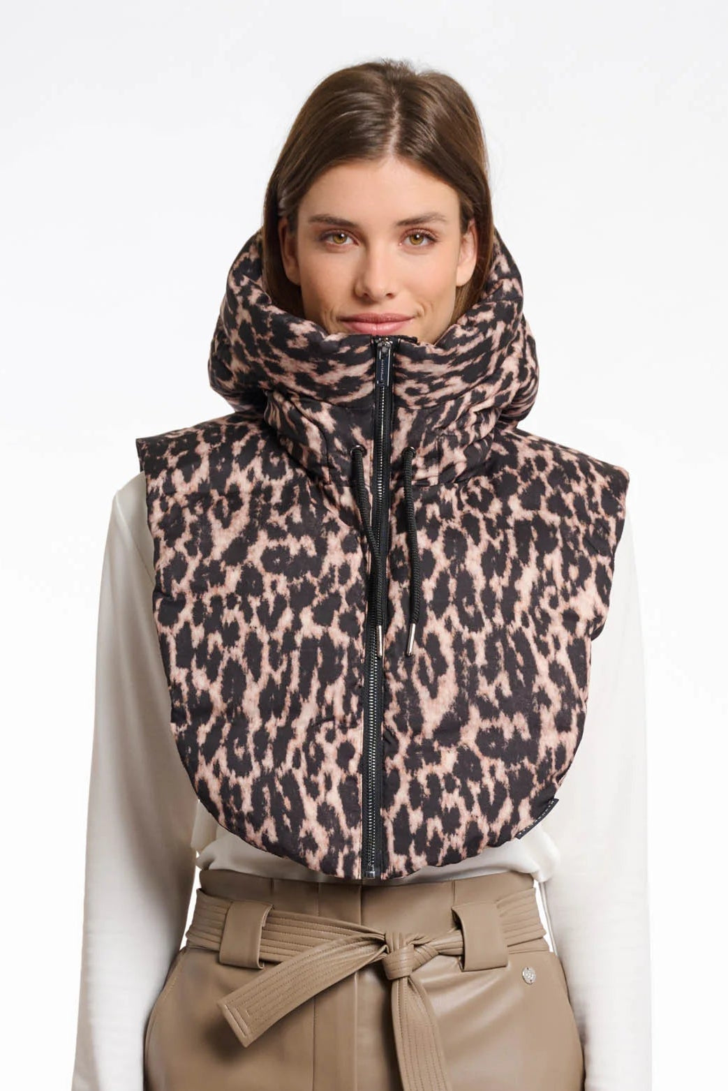 Woman wearing a leopard print vest over a white shirt and beige pants on a white background