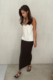 Woman wearing a white top and brown skirt against a white wall.