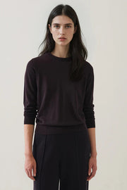 Woman wearing a dark purple sweater and pants against a plain background