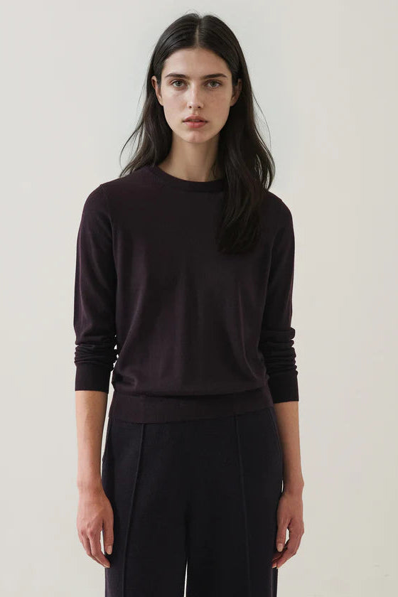 Woman wearing a dark purple sweater and pants against a plain background