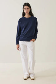 Person wearing a navy oversized sweater and white pants on a plain background
