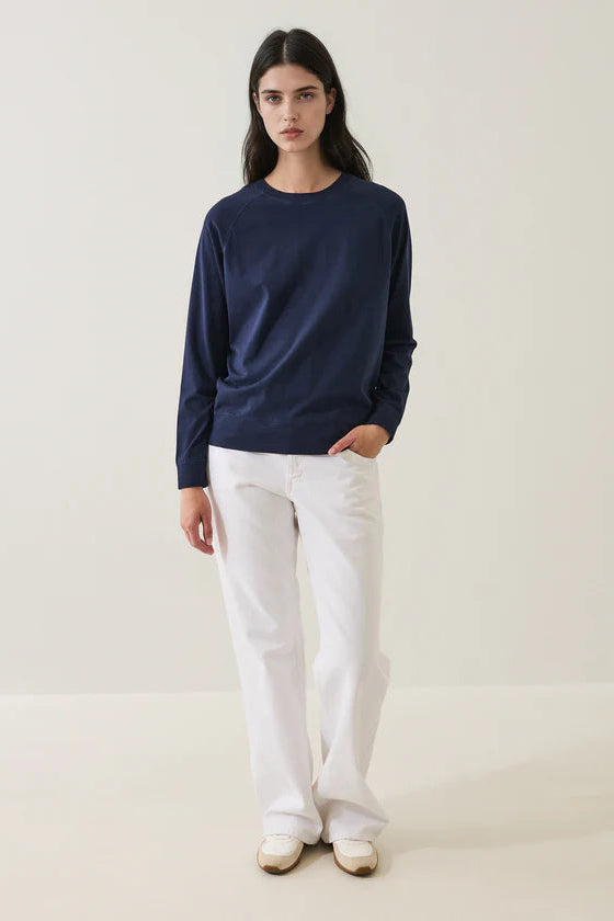 Person wearing a navy oversized sweater and white pants on a plain background