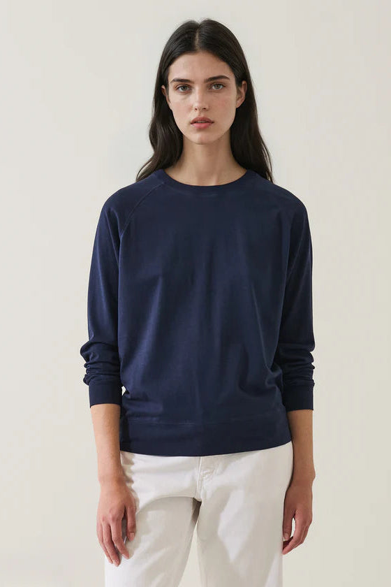 Woman wearing an oversized navy sweater and white pants on a plain background