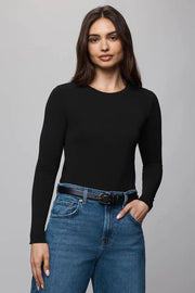 Woman wearing a black long-sleeve top and blue jeans on a gray background