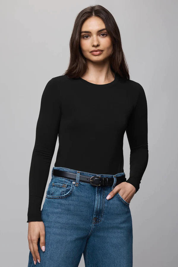 Woman wearing a black long-sleeve top and blue jeans on a gray background