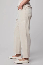 Side view of a person wearing oat-coloured corduroy pants and white sneakers on a plain background