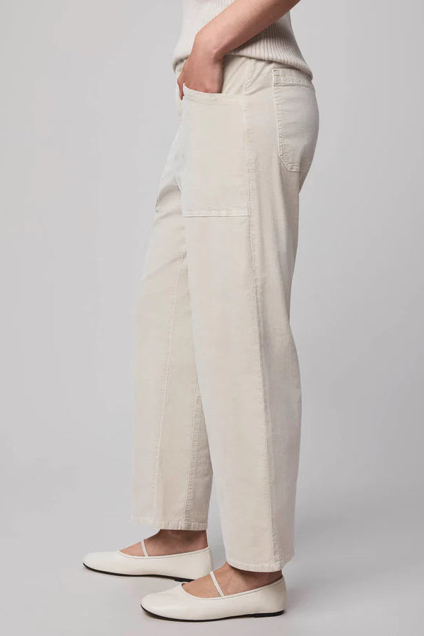 Side view of a person wearing oat-coloured corduroy pants and white sneakers on a plain background