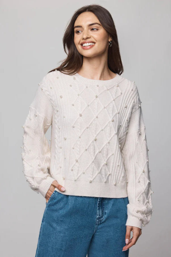 Woman wearing a cream sweater with cable knit pattern and pearl detailing all over