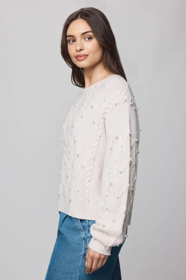 Woman wearing a cream sweater with cable knit pattern and pearl detailing all over