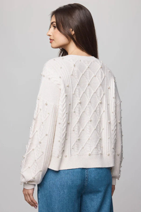 Woman wearing a cream sweater with cable knit pattern and pearl detailing all over