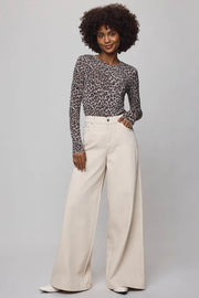 Woman wearing a patterned top and wide-leg pants on a plain background