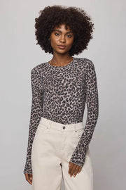 Woman wearing a leopard print long-sleeve top and white pants against a gray background