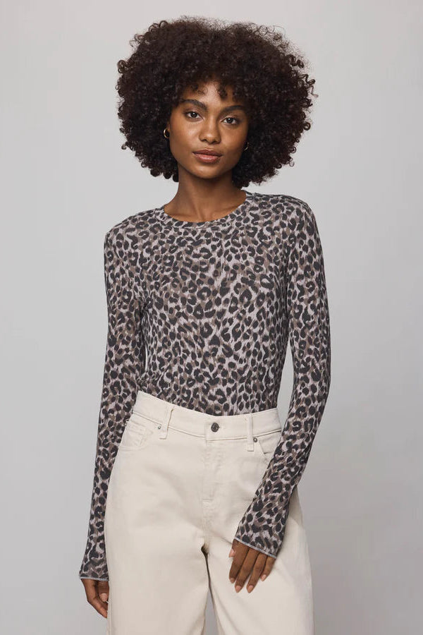 Woman wearing a leopard print long-sleeve top and white pants against a gray background