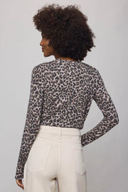 Person wearing a leopard print long-sleeve top and white pants on a plain background