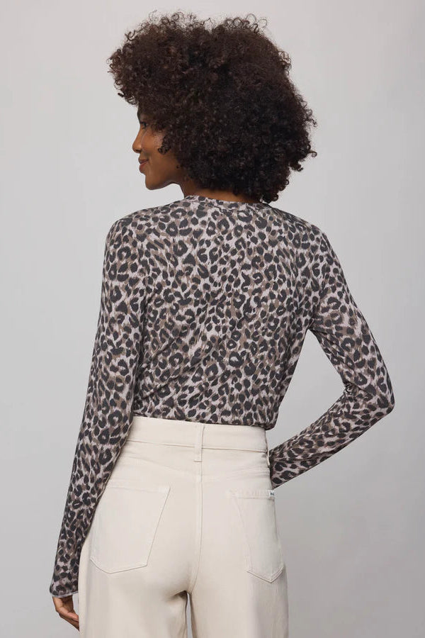 Person wearing a leopard print long-sleeve top and white pants on a plain background