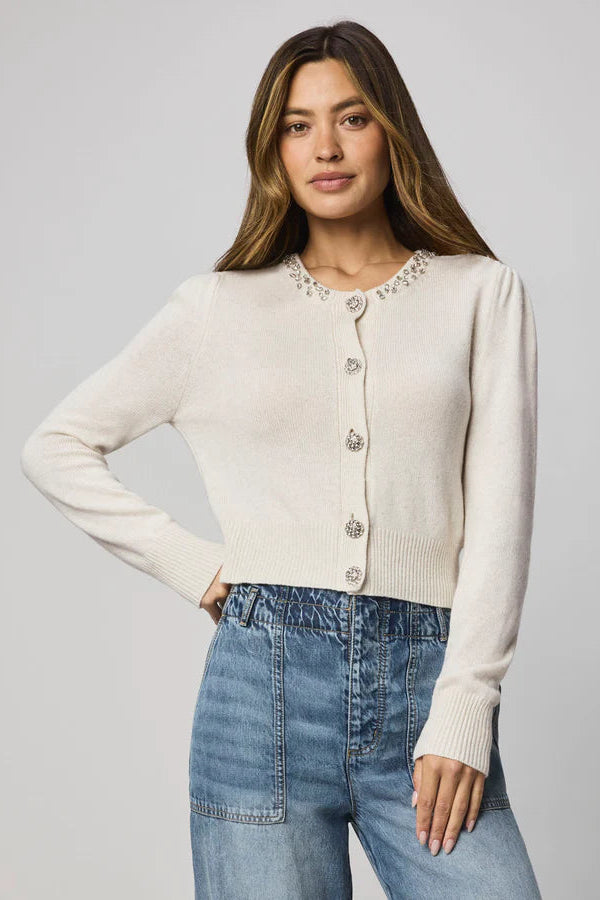 Woman wearing a beige cardigan with decorative buttons and embellishments on the collar 