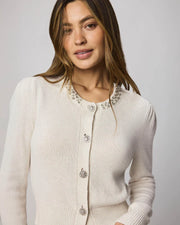 Woman wearing a beige cardigan with decorative buttons and embellishments on the collar 