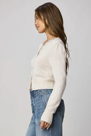 Woman wearing a beige cardigan with decorative buttons and embellishments on the collar 