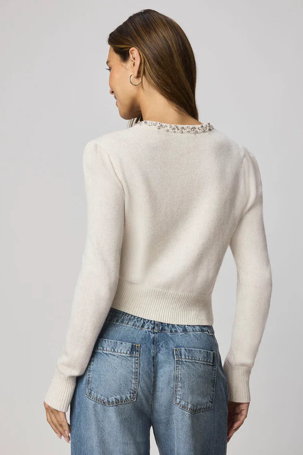 Woman wearing a beige cardigan with decorative buttons and embellishments on the collar 