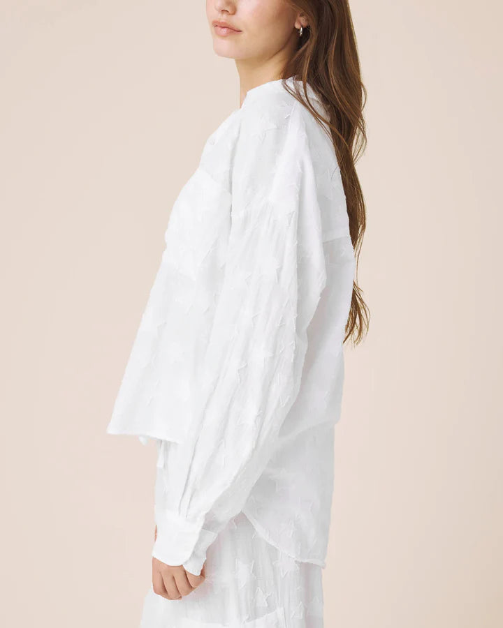 Woman wearing white button up top with star details 