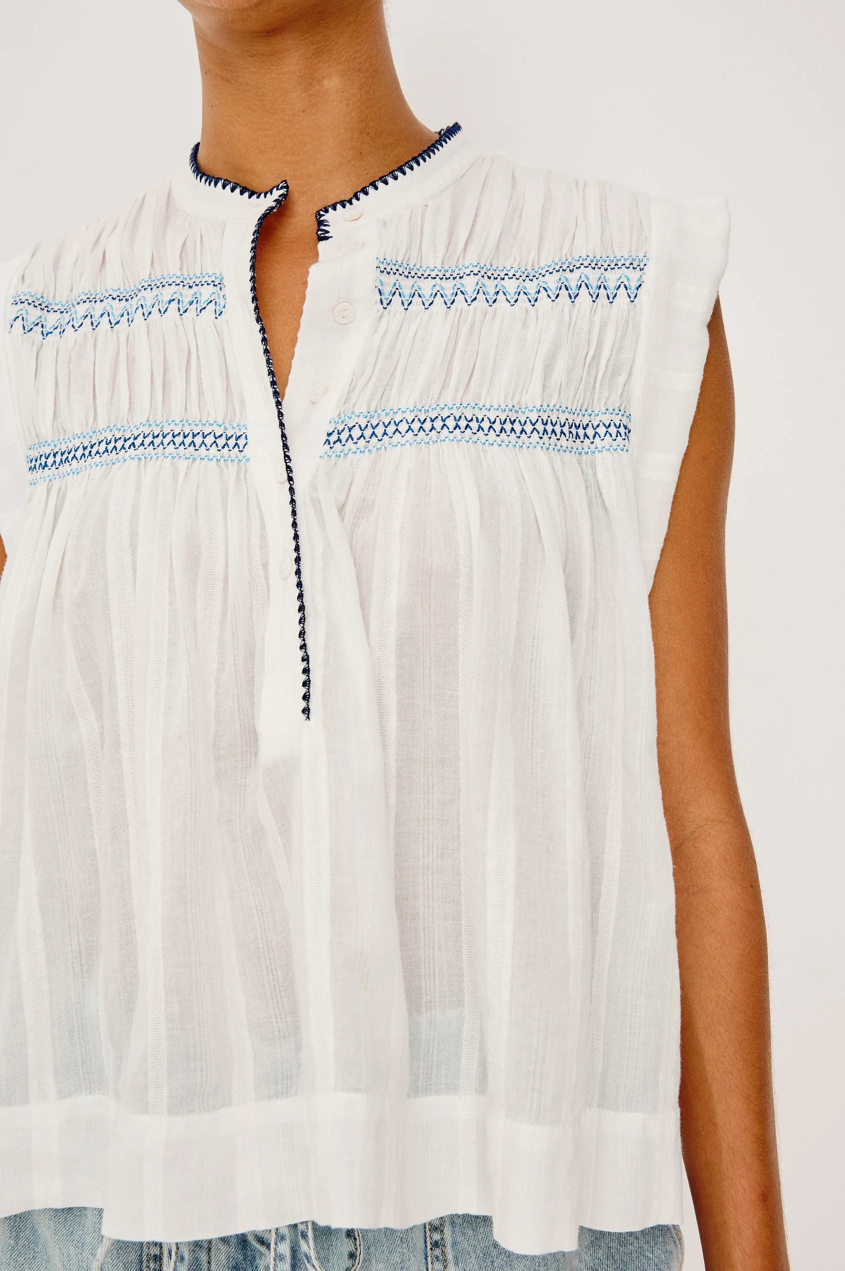 Woman wearing a flowy sleeveless white top with blue embroidery 